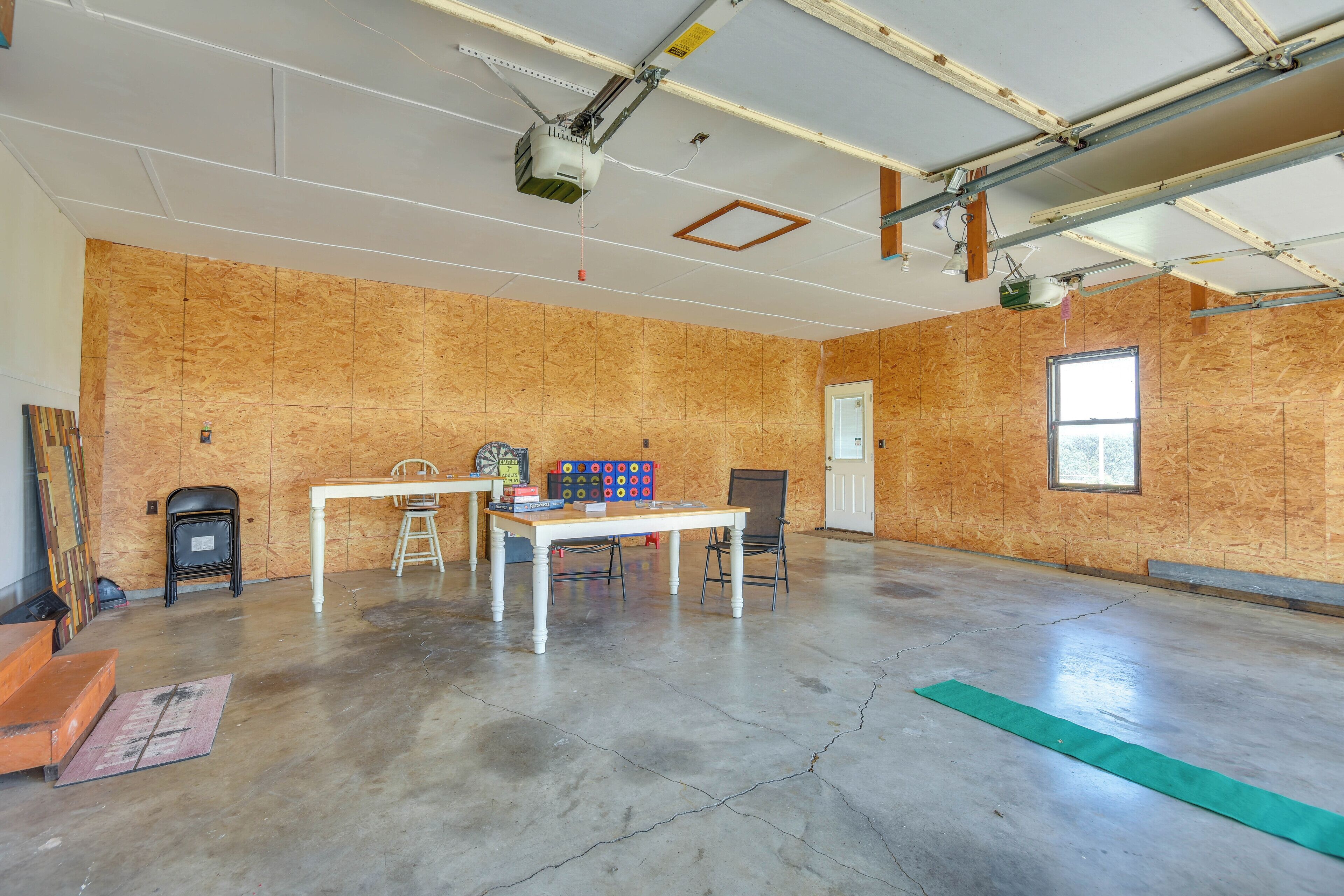 Una habitación amplia con techo alto, paredes de madera a la vista, suelo de hormigón, una mesa con sillas y un proyector montado en el techo.