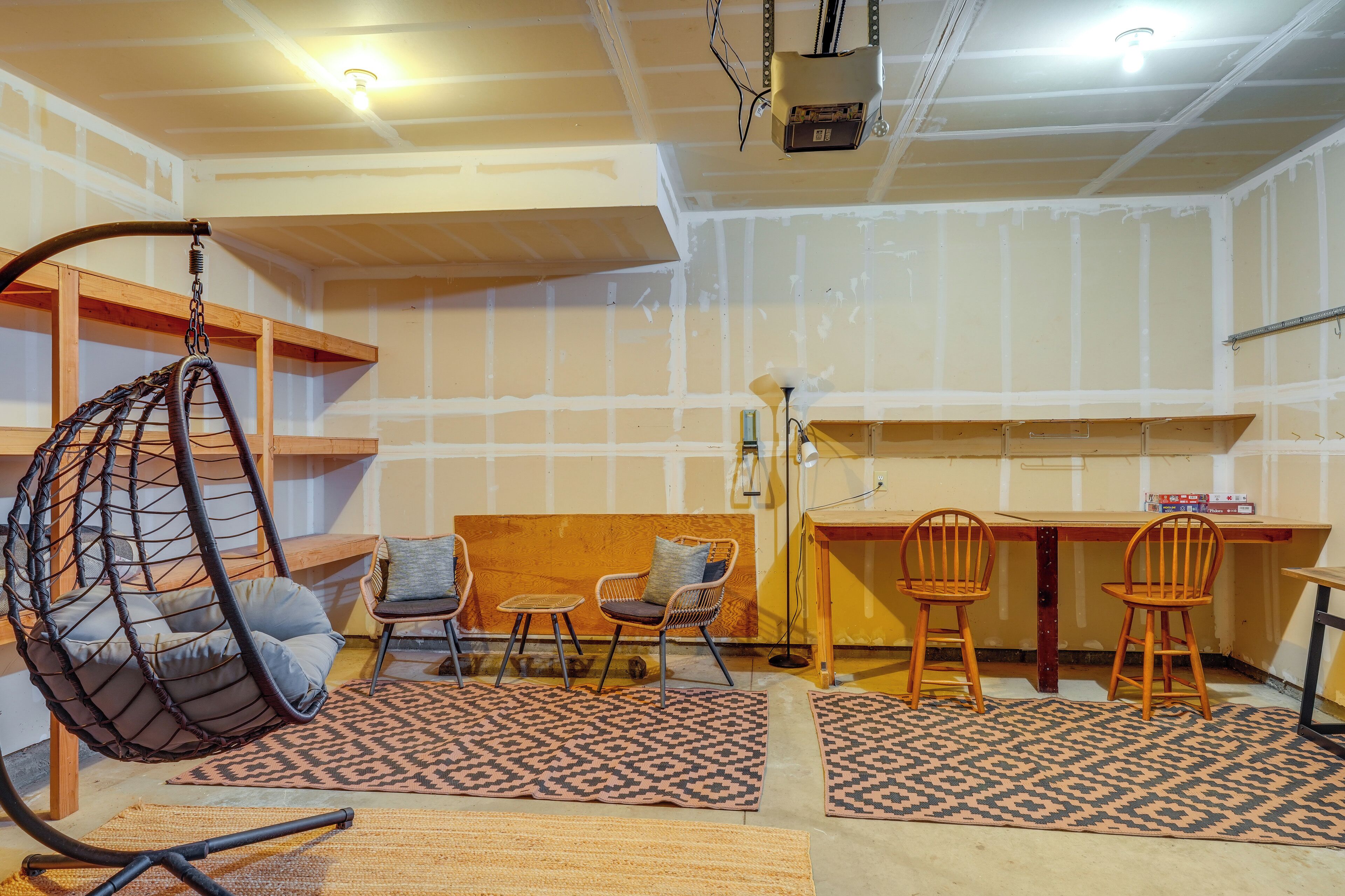 Une pièce avec un fauteuil suspendu, une table en bois et deux chaises.