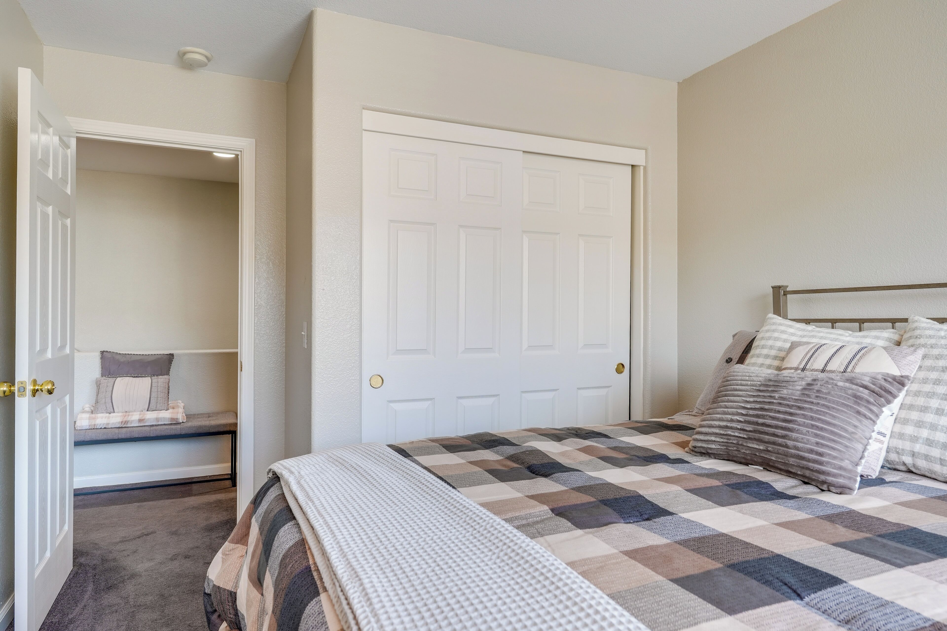 A bedroom with a bed, a closet, and a bench with pillows.