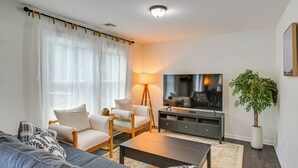 Ein Wohnzimmer mit einer Couch, Sesseln, einem Couchtisch, einem Fernseher, einer Lampe und einer Pflanze.