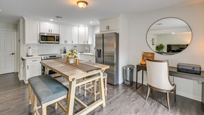 A modern kitchen with white cabinets, stainless steel appliances, a wooden dining table, and a round mirror. - Walk to Train! Updated Apt in Huntington Station (Huntington Station)