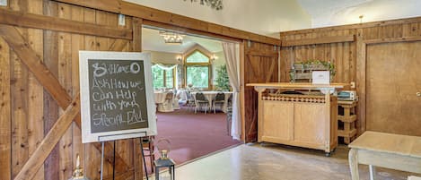 A rustic interior with a chalkboard sign, wooden walls, and a view into a dining area.