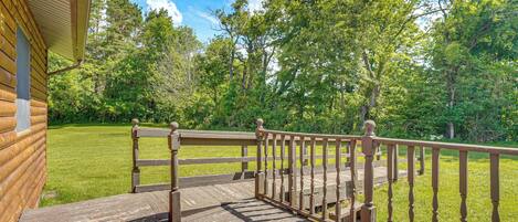 A wooden deck with a railing, leading to a grassy area with trees.