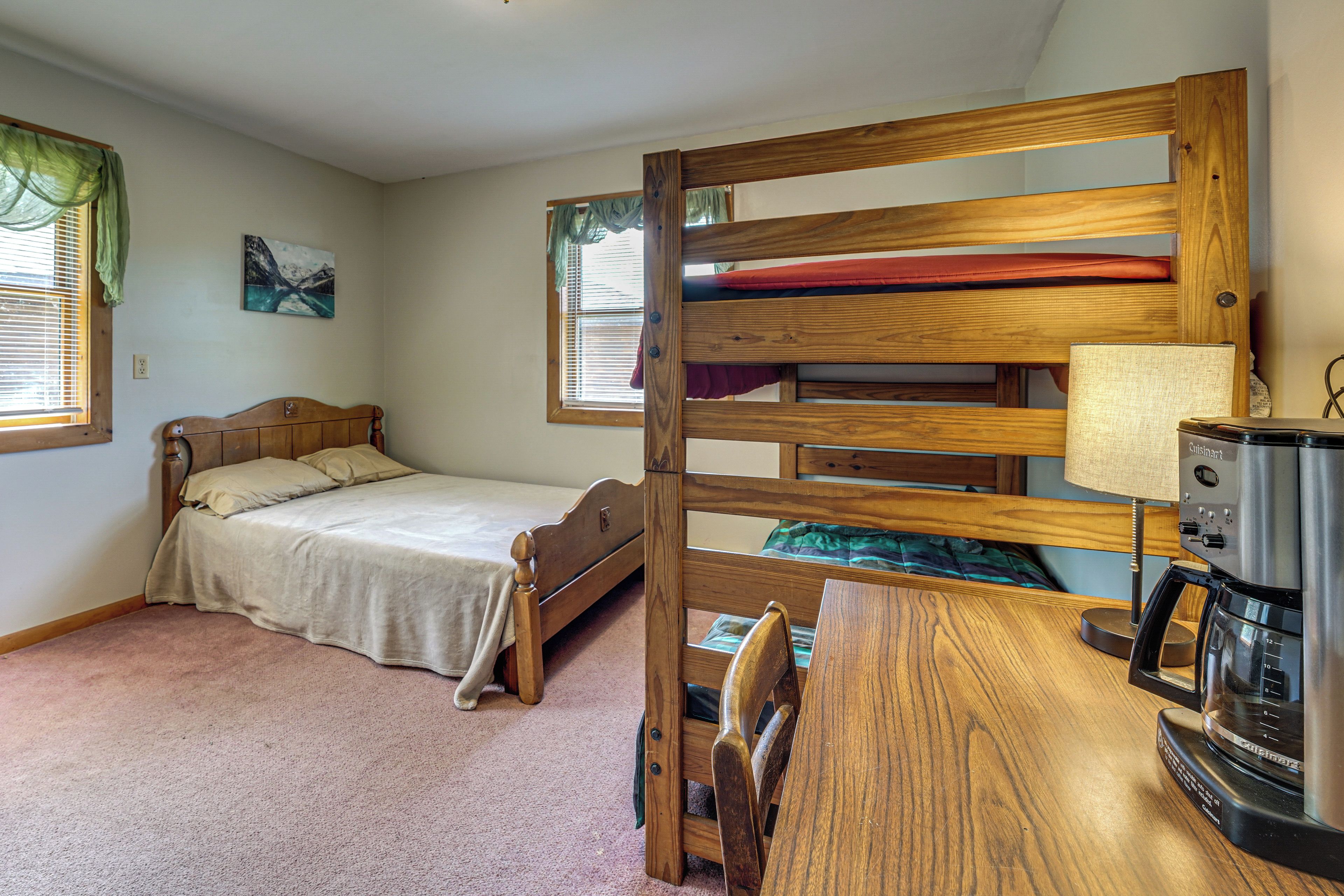 A bedroom with a bunk bed, a desk with a lamp, and a kitchenette area.
