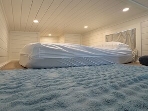 A bedroom with a bed covered in white sheets, a blue textured blanket, and a wooden ceiling with recessed lighting. - Oceanfront Tiny Retreat On Wheels, Fall Package + 2 Bikes (Holden Beach)