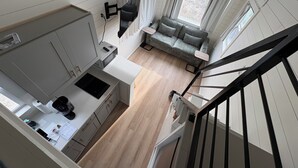A compact living space with a kitchenette, a sofa, and a staircase. - Oceanfront Tiny Retreat On Wheels, Fall Package + 2 Bikes (Holden Beach)