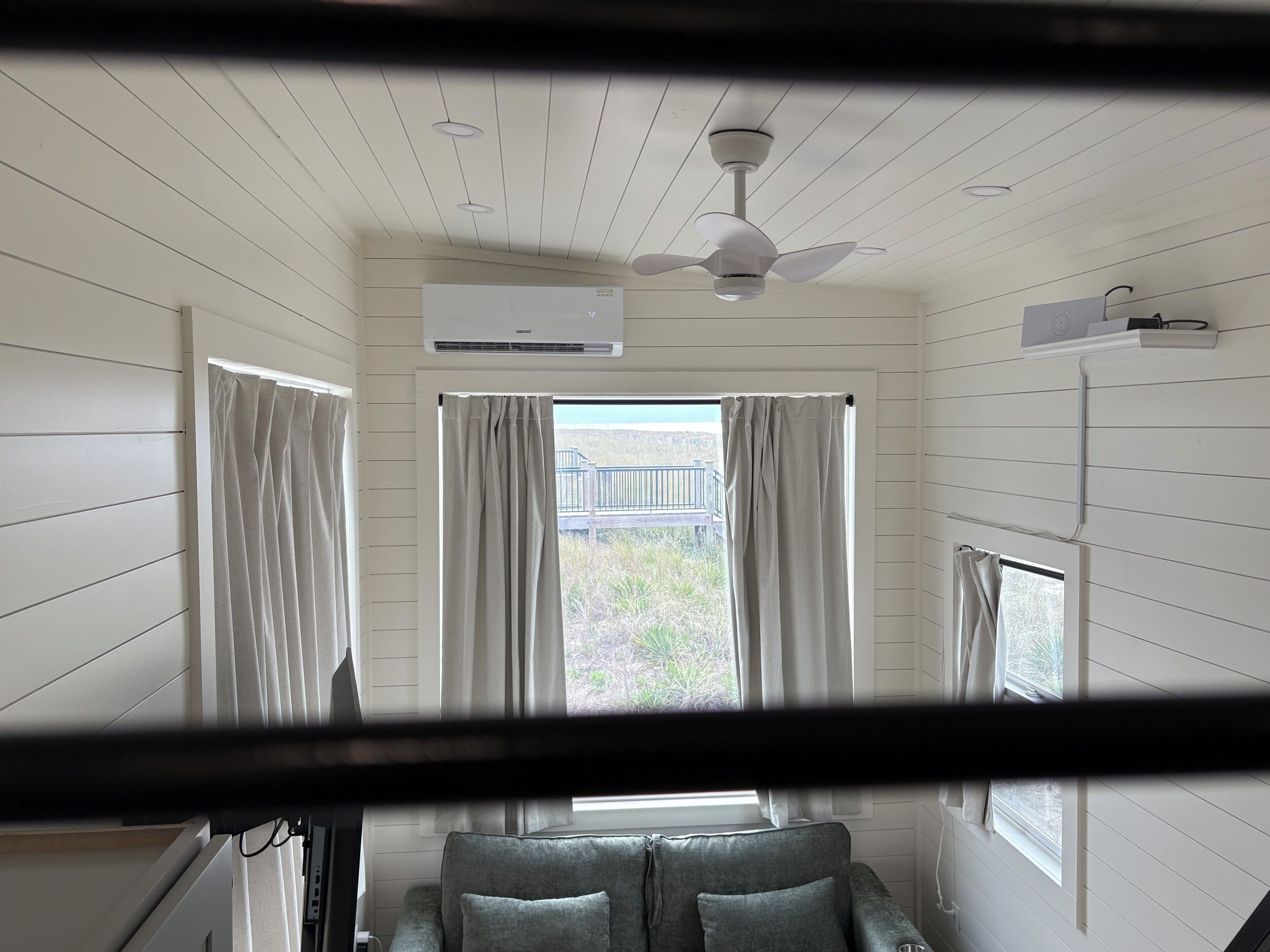 Een kamer met plafondventilator, airconditioning en een raam met gordijnen.
