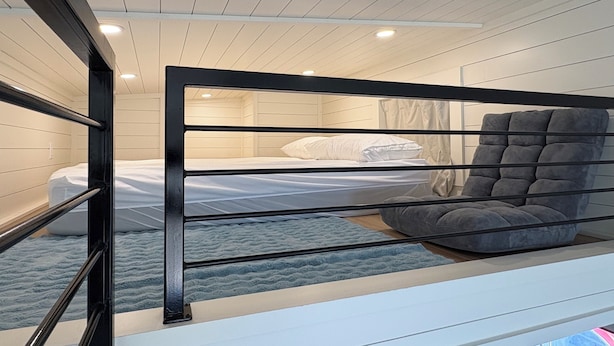 A bunk bed with a grey upholstered headboard, white bedding, and a blue textured rug. - Oceanfront Tiny Retreat On Wheels, Fall Package + 2 Bikes (Holden Beach)