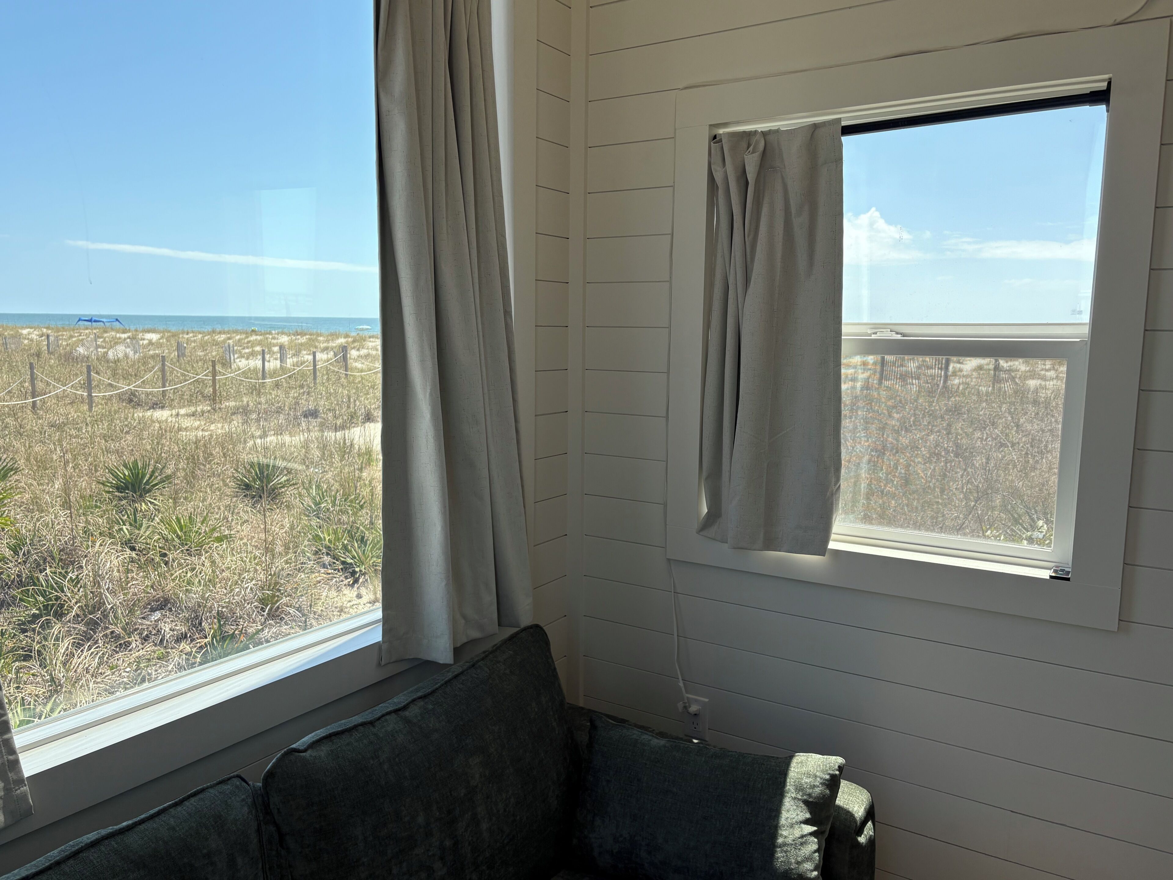 A room with a window overlooking a beach, a couch, and a curtain.