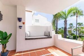 A balcony with a built-in bench, a potted plant, and a view of palm trees and buildings. - Costalita 2BR, Pool, Garage & Direct Beach Access (Estepona)