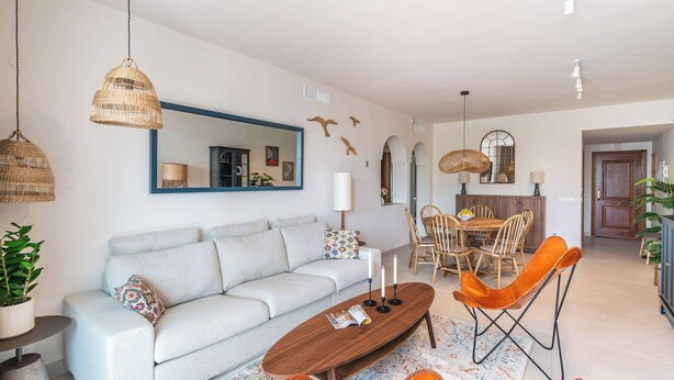 Un salon moderne avec un canapé, une table basse et des fauteuils orange. On y trouve également un coin repas avec une table et des chaises en bois.
