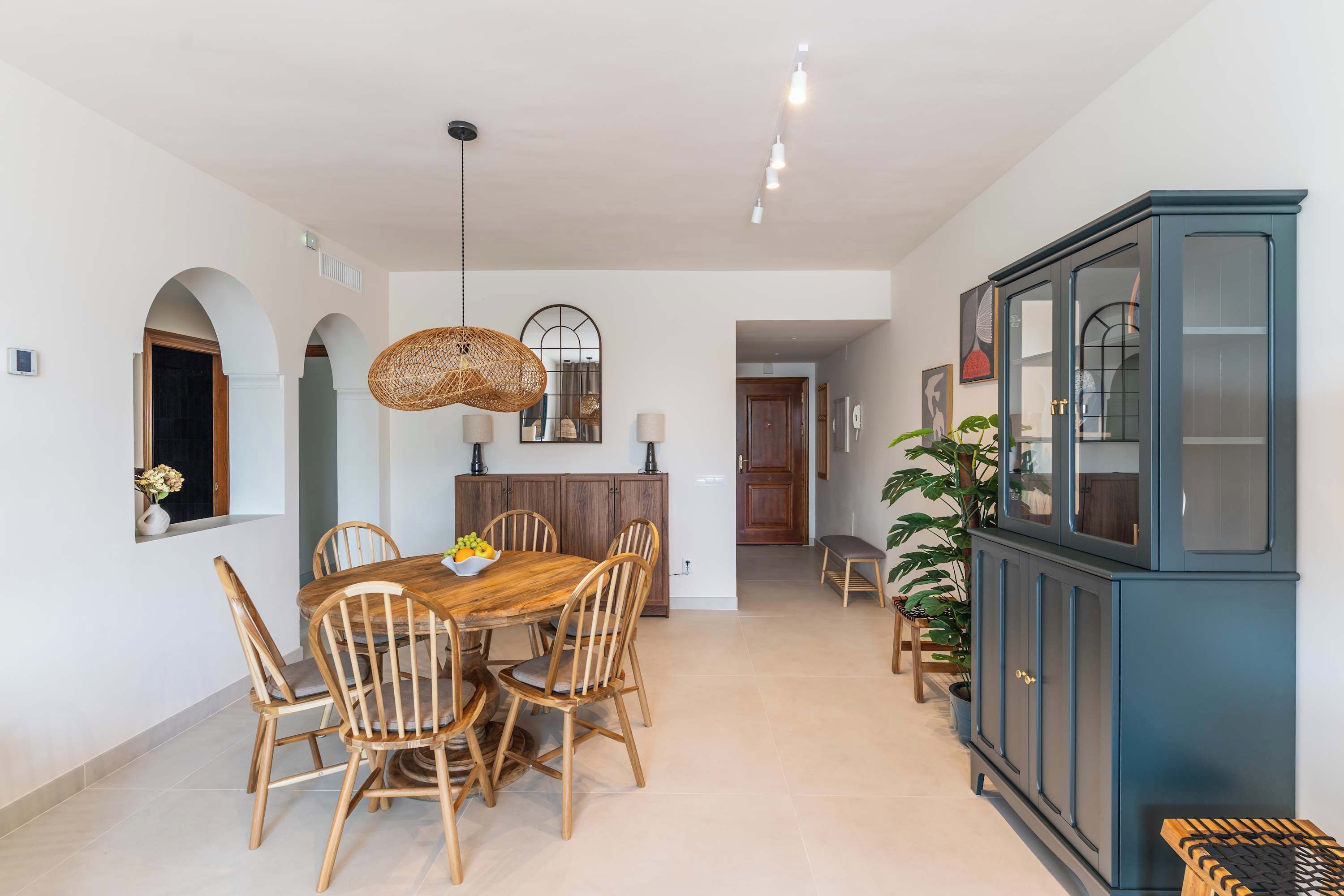 Un comedor con una mesa redonda de madera, seis sillas, una lámpara colgante y un armario azul con puertas de cristal.
