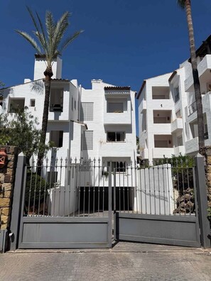 A multi-story residential building with a gated entrance, balconies, and a palm tree. - Costalita 2BR, Pool, Garage & Direct Beach Access (Estepona)