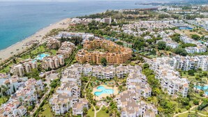 Un quartier résidentiel situé sur la côte, avec un ensemble d’immeubles d’appartements au centre, une plage et une piscine.