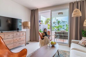 A modern living room with a flat-screen TV, a leather armchair, a sofa, and a dining table. - Costalita 2BR, Pool, Garage & Direct Beach Access (Estepona)
