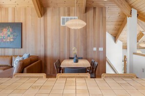 A wooden-paneled room with a dining table, chairs, a hanging light fixture, and a painting on the wall. - Unit 35C Lot 8 Oceanhaus (The Sea Ranch)