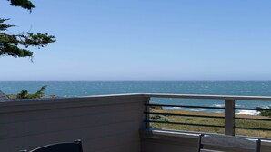 Uma varanda com vista para o oceano, uma mesa e duas cadeiras.