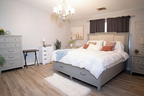 Un dormitorio con cama, cómoda, mesita de noche y una araña.