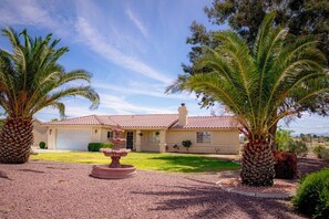 A house with a red-tiled roof, a front yard with palm trees, and a gravel driveway.