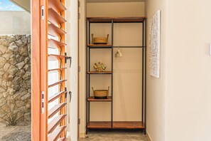 A hallway with a wooden door, a stone wall, and a metal-framed shelving unit with baskets and a decorative item. - NEW luxury vacation villa with a pool next to Jan Thiel Beach (Jan Thiel)