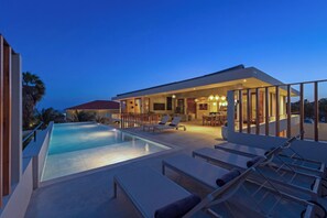 A modern poolside area with lounge chairs and a dining area, overlooking a residential building. - NEW luxury vacation villa with a pool next to Jan Thiel Beach (Jan Thiel)