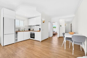 A modern kitchen with white cabinetry, a wooden countertop, and a dining area with a white table and grey chairs. - Home Holidays 152 (San Miguel de Abona)
