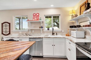 A modern kitchen with white cabinets, a wooden table, a dishwasher, and a microwave. - Westview Lookout | Panoramic Lake Views, Decks & Near Boat Ramp (Canyon Lake)