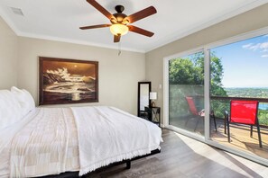 Ein Schlafzimmer mit einem großen Bett, einem Deckenventilator, einem Gemälde, einem Nachttisch und Blick durch eine Glasschiebetür auf eine Außenterrasse.