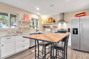 Eine moderne Küche mit weißen Schränken, einem Holztisch, schwarzen Barhocker, einem Edelstahlkühlschrank und einer roten Doppeldeckerbus-Dekoration.