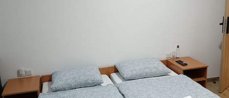 A double bed with patterned bedding, two bedside tables, a painting on the wall, and a wooden wardrobe.