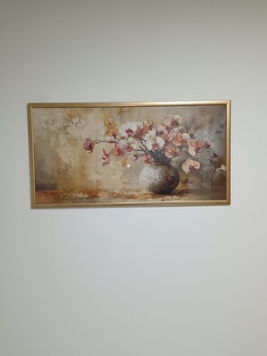 A framed artwork of flowers in a vase on a wall.