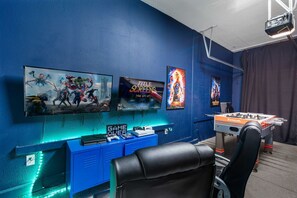 A room with a blue wall, a mounted TV, a foosball table, and a gaming chair. - Private Pool+Spa*Games Room*Clubhouse Amenities (Kissimmee)