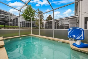 An indoor pool with a basketball hoop, surrounded by a glass enclosure with trees visible outside. - Private Pool+Spa*Games Room*Clubhouse Amenities (Kissimmee)