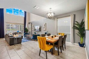 A spacious living area with a dining table set for six, a sofa, and a large window with curtains. - Private Pool+Spa*Games Room*Clubhouse Amenities (Kissimmee)