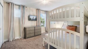Een kinderkamer met stapelbedden, een dressoir en een raam met gordijnen.