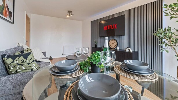 A modern living room with a dining area, a flat-screen TV, and a clock on the wall. - 2 Bed Apartment - Sleeps 5 - Parking - Wifi (Birmingham)