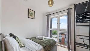 A bedroom with a bed, a window, a hanging light fixture, and a wall-mounted rack. - 2 Bed Apartment - Sleeps 5 - Parking - Wifi (Birmingham)