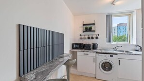 A modern kitchen with a built-in washing machine, a sink, and a window with a city view. - 2 Bed Apartment - Sleeps 5 - Parking - Wifi (Birmingham)