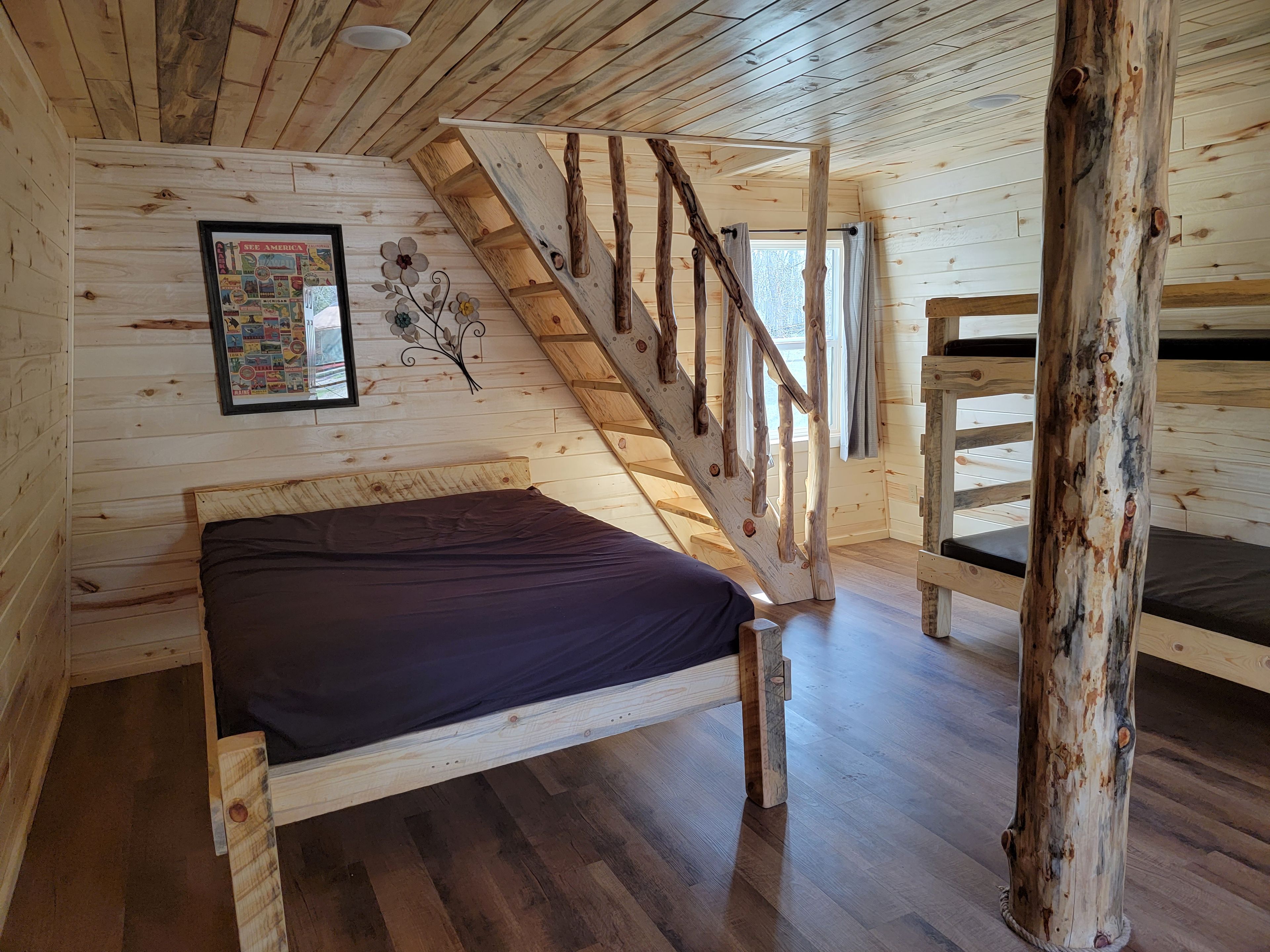 A cabin interior with a wooden bed, a staircase, and a wall-mounted poster.