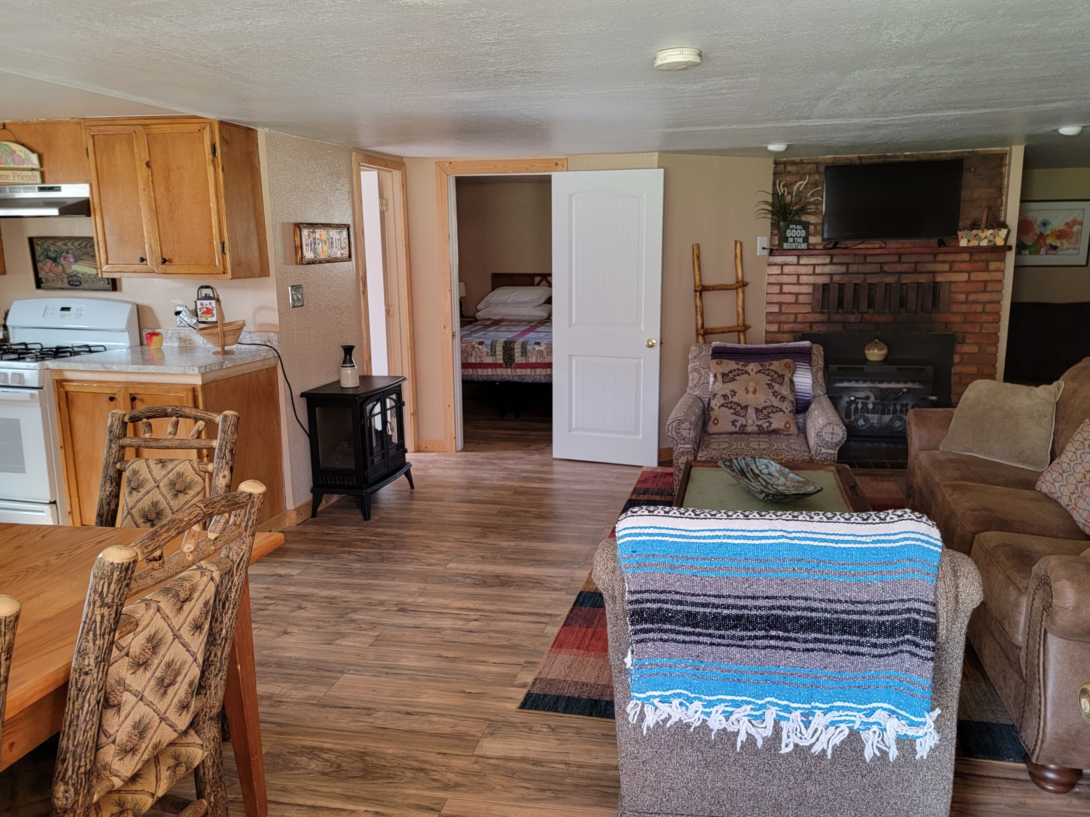 A cozy living room with a fireplace, a dining area with wooden furniture, and a kitchen with a stove.