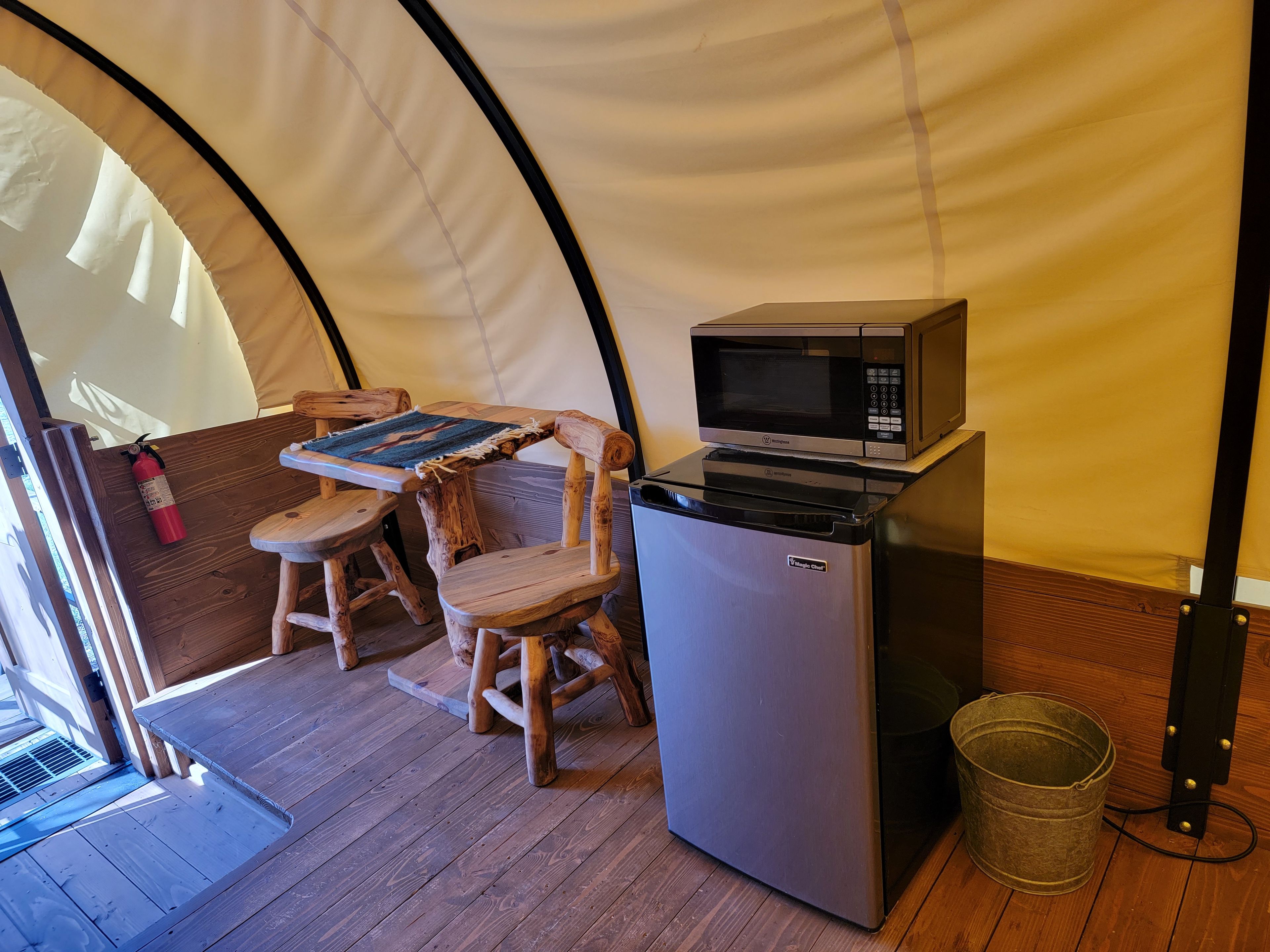 A compact kitchenette with a microwave, a small refrigerator, and a wooden table with chairs.