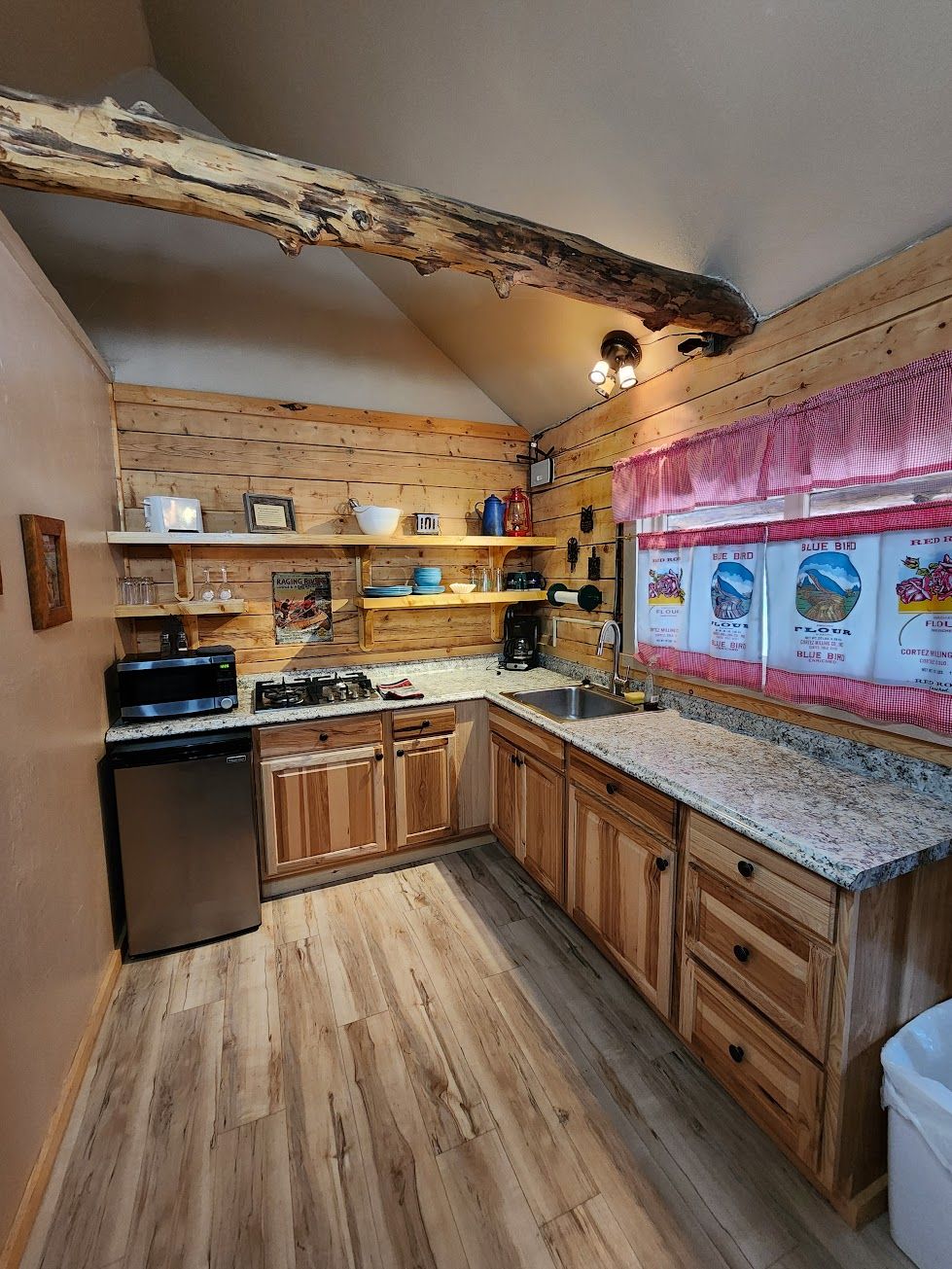 A compact kitchen with wooden cabinets, a granite countertop, and a rustic ceiling beam.