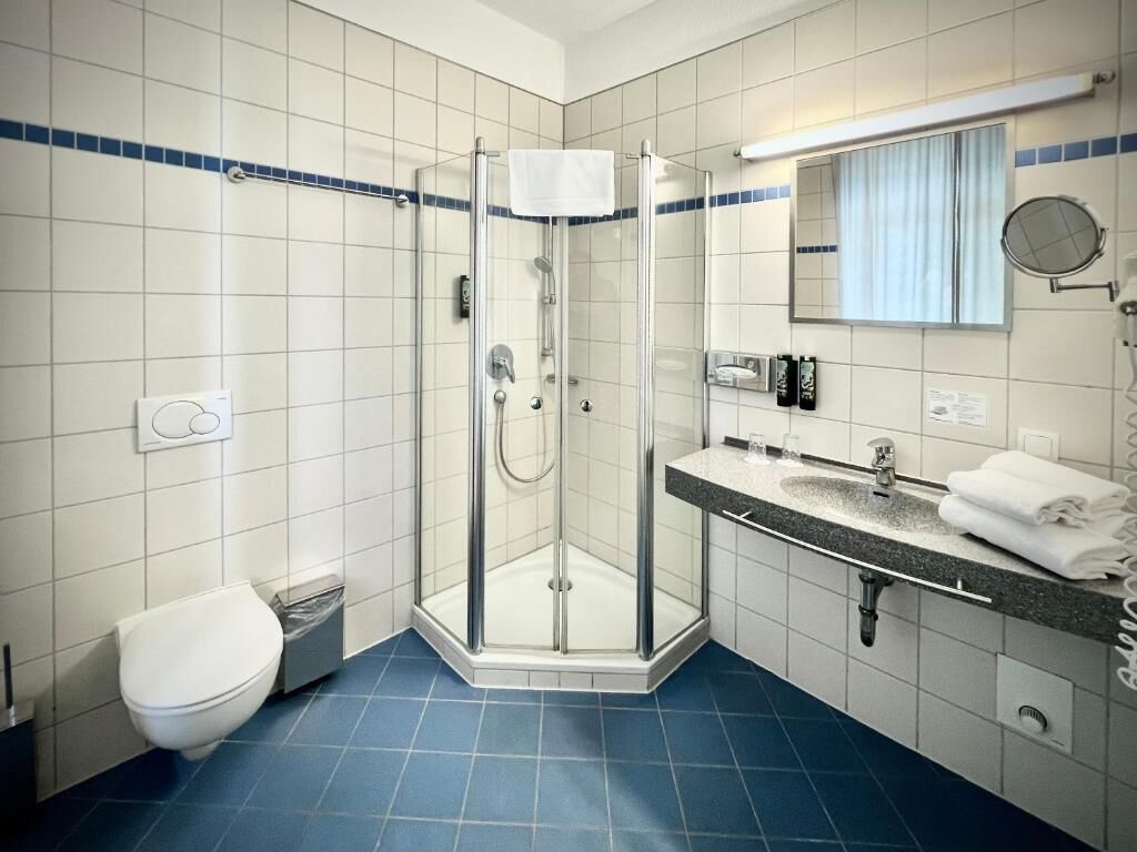 Un baño moderno con ducha de vidrio, inodoro blanco y lavamanos con espejo arriba.