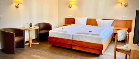 Habitación de hotel con cama doble, dos mesitas de noche, una silla, una mesita con lámpara y un televisor.