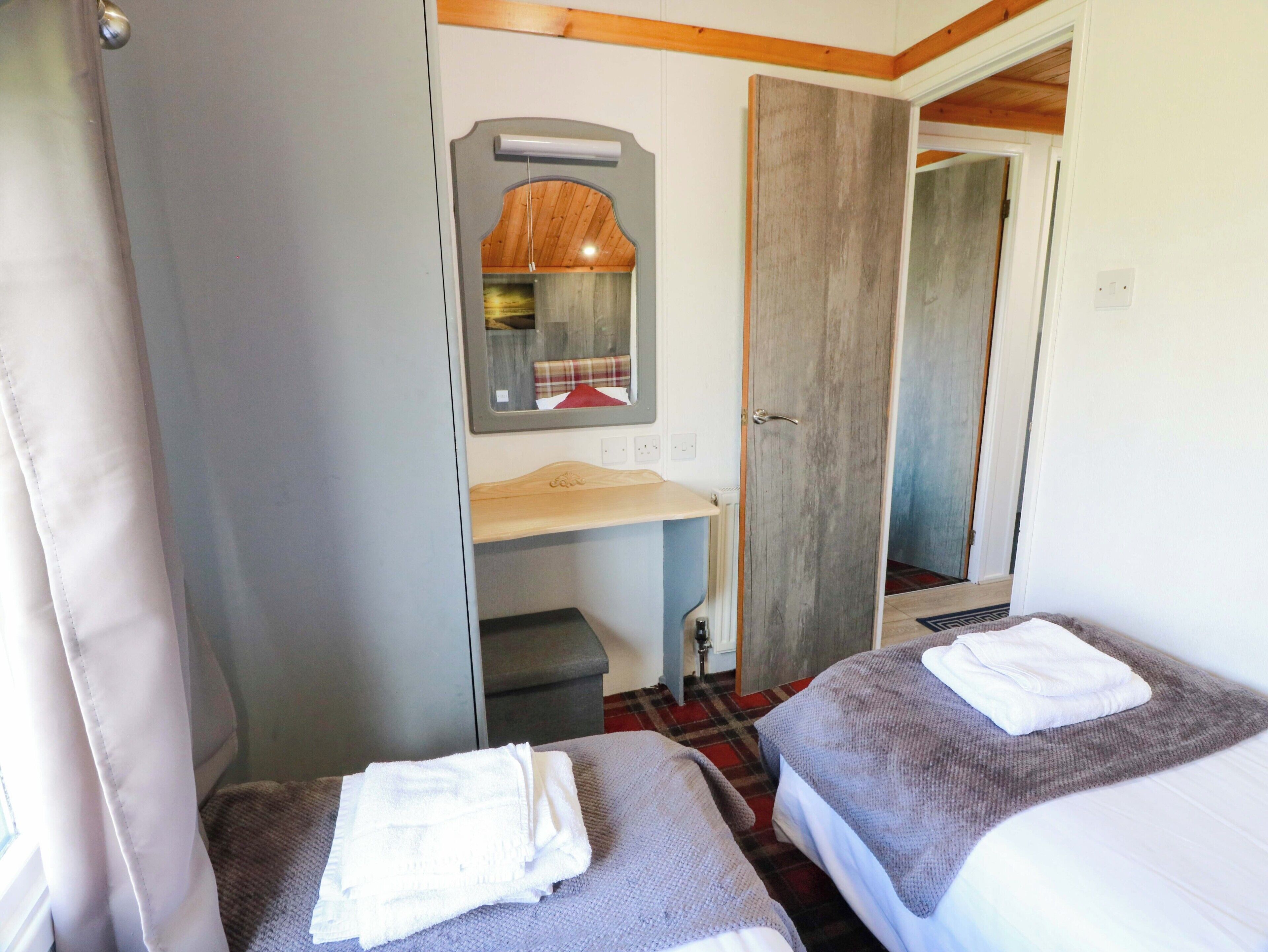 A room with two beds, a small desk, a mirror, and a wardrobe.