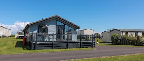 A mobile home with a balcony, a fenced yard, and a clear sky.