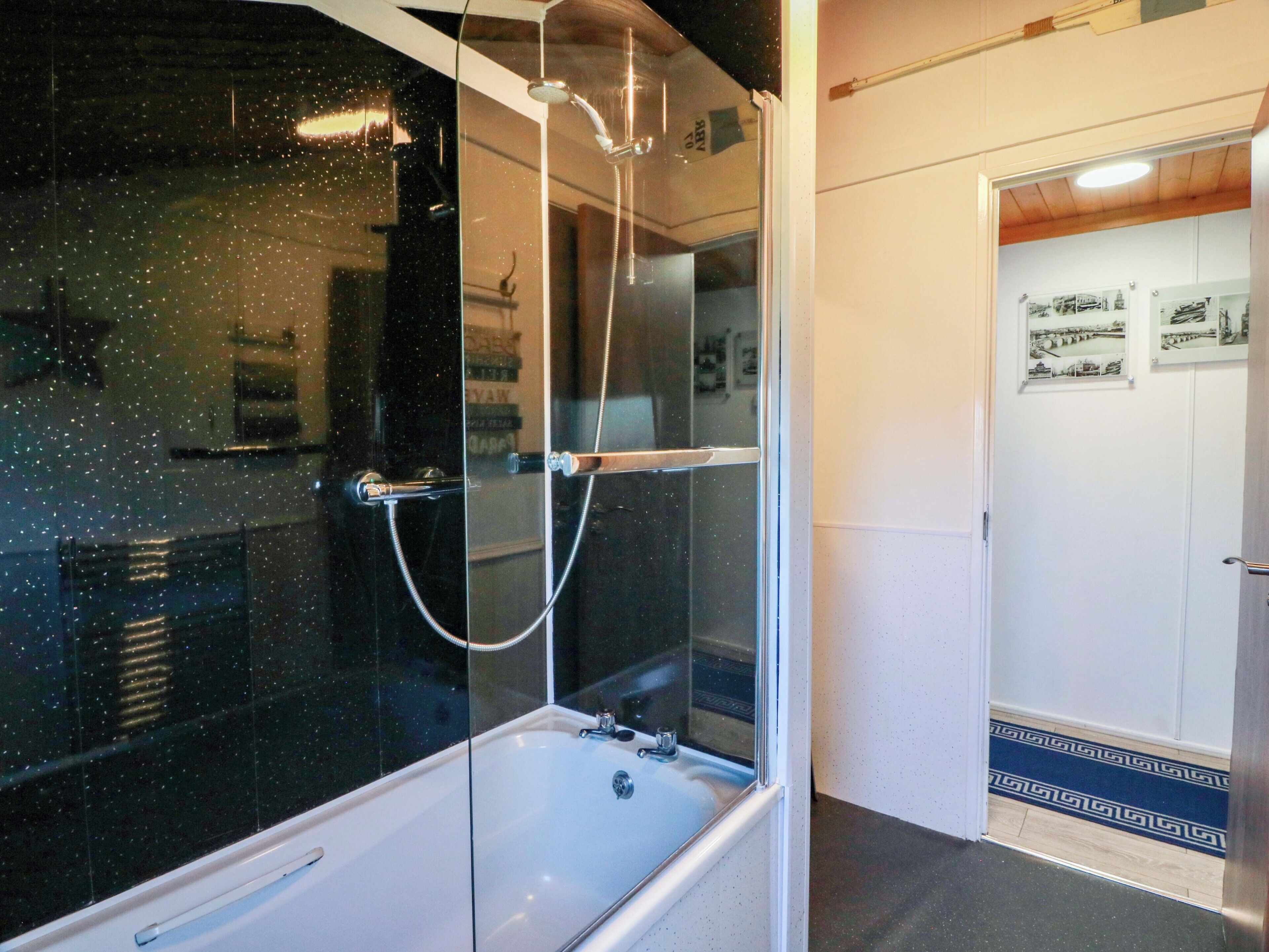 A bathroom with a glass-enclosed shower, a white bathtub, and a door with framed pictures.