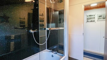A bathroom with a glass-enclosed shower, a white bathtub, and a door with framed pictures.