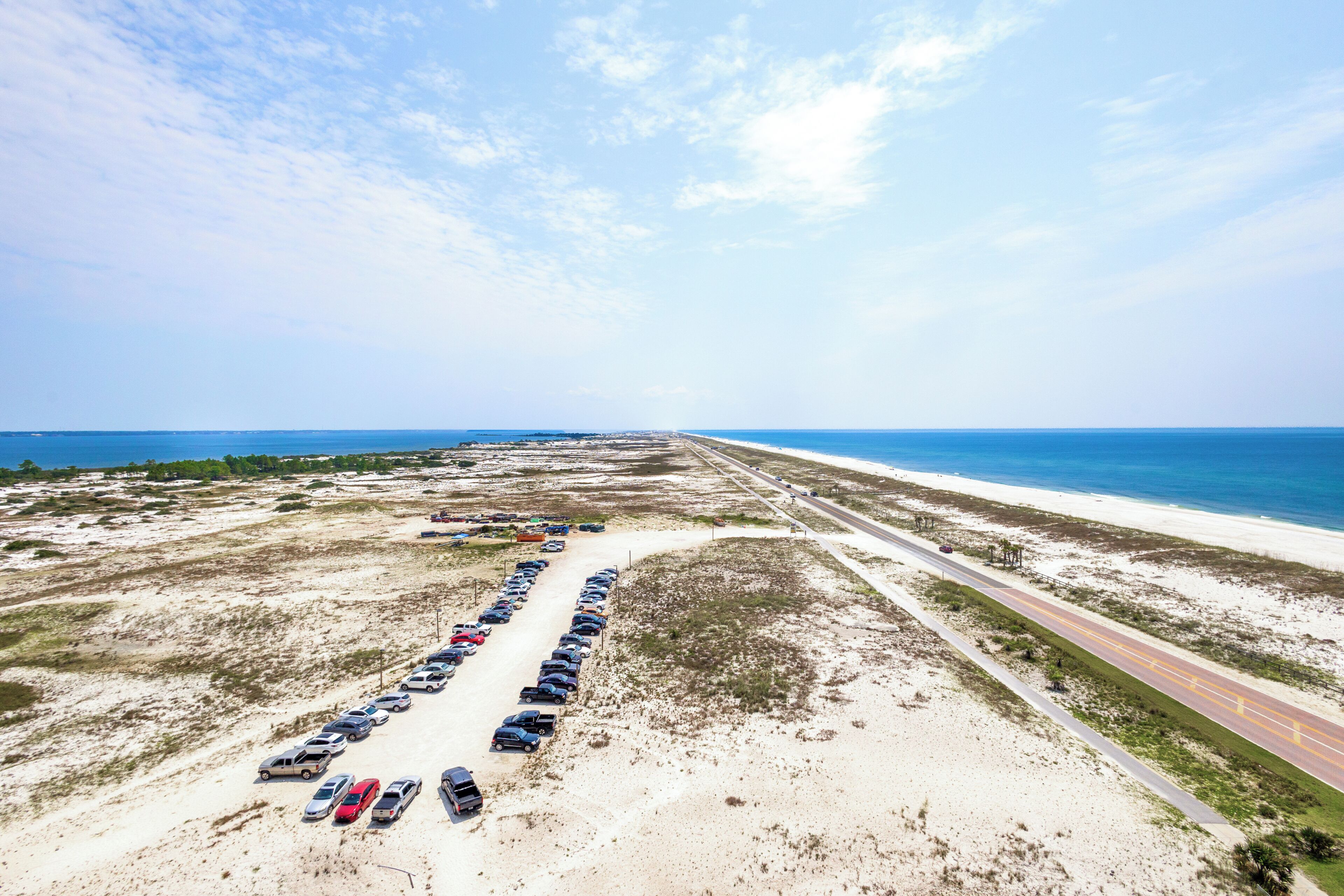 Luchtbeeld van een kustweg met een lange rij geparkeerde auto's en een strand aan de rechterkant.