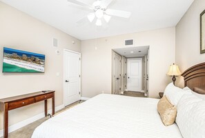 A hotel room with a bed, a desk, a ceiling fan, a painting of a beach, and a view of the ocean. - Portofino Tower 3-1009 | Gulf Views & Steps to the Beach (Pensacola Beach)